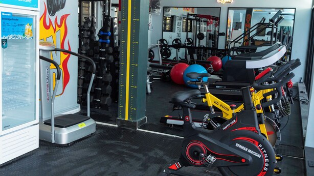 Un gimnasio con equipo de ejercicio, una báscula y un refrigerador para bebidas.