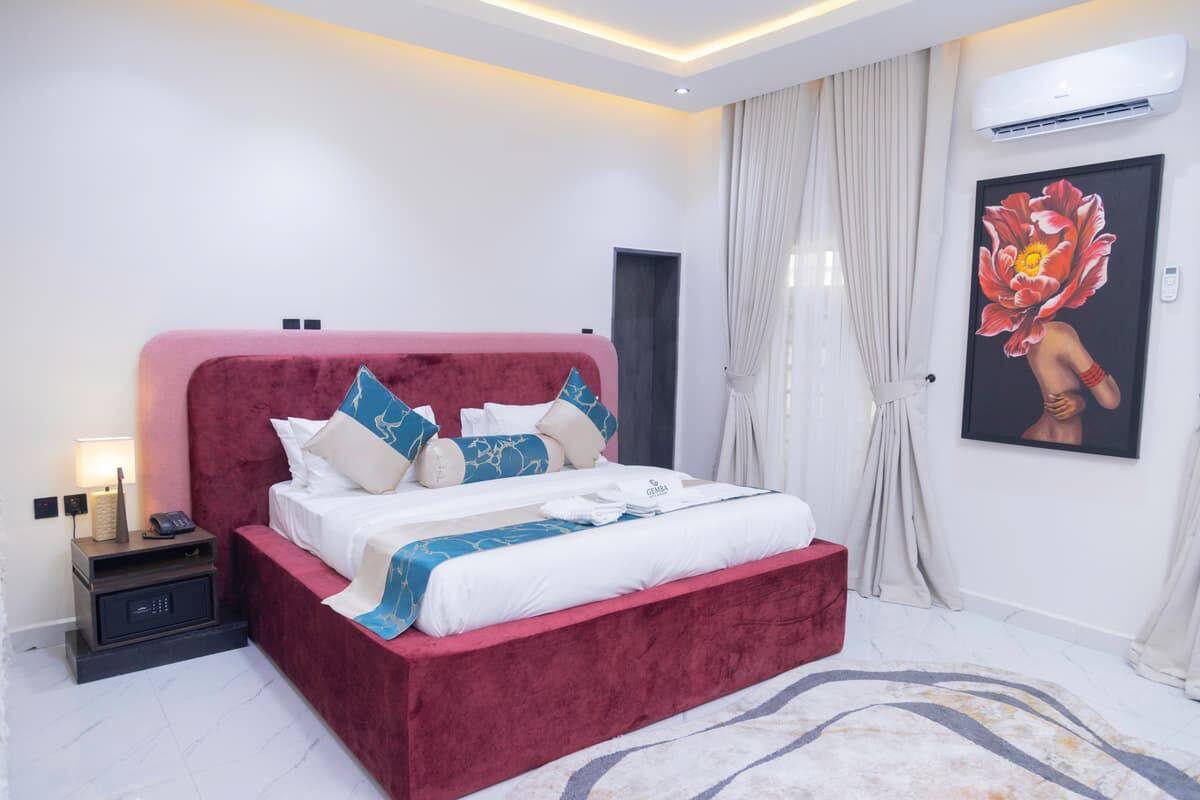Ein modernes Hotelzimmer mit einem rot gepolsterten Bett, einem Nachttisch mit Lampe und einem großen floralen Kunstwerk an der Wand.