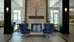 A lobby with a stone fireplace, two blue chairs, and a seating area with tables and chairs. - 1BR Two-Queen Suite + Sofa Bed in St. Pete (St. Petersburg)