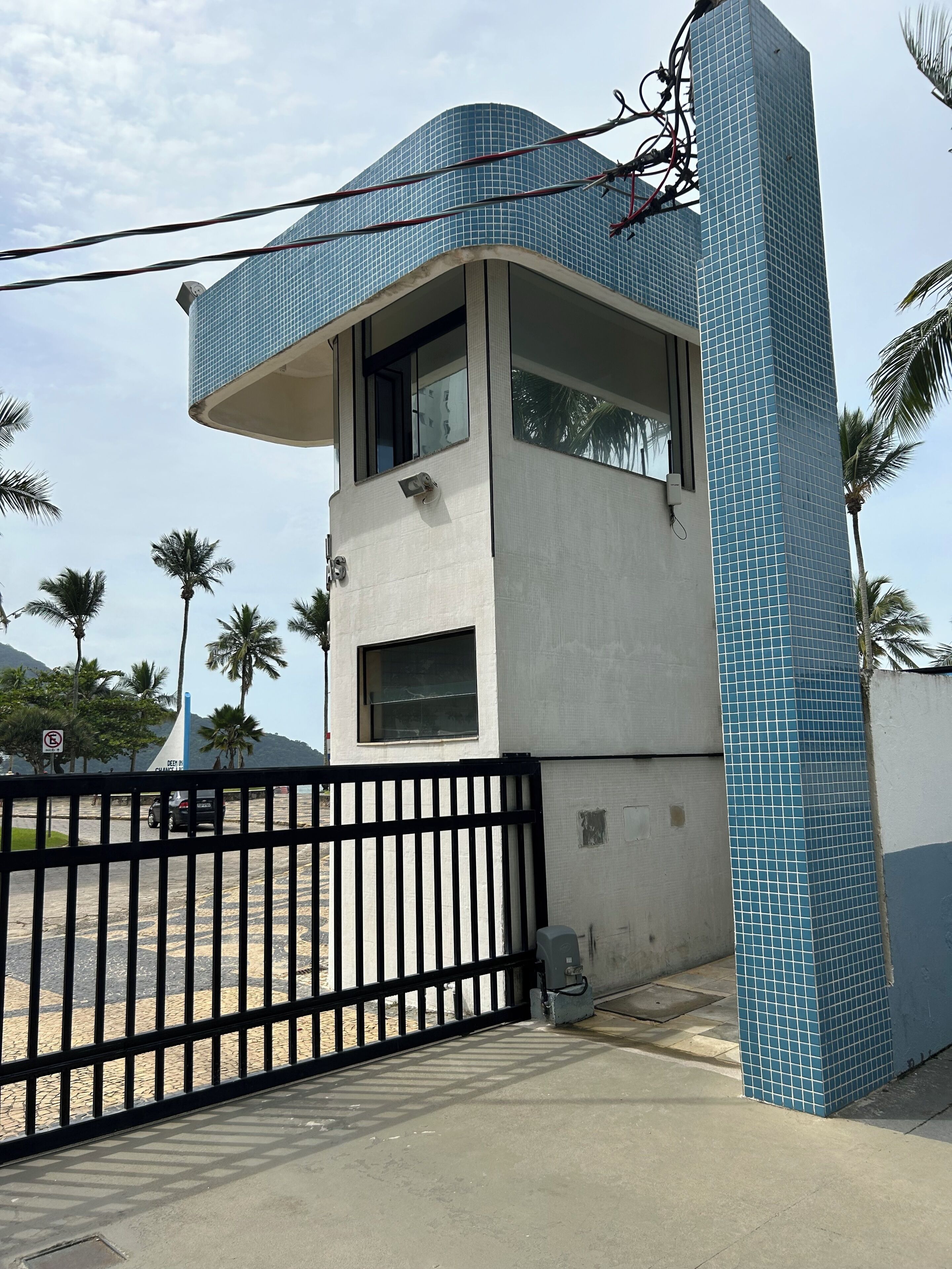 A modern building with a curved glass facade, a gated entrance, and palm trees in the background.