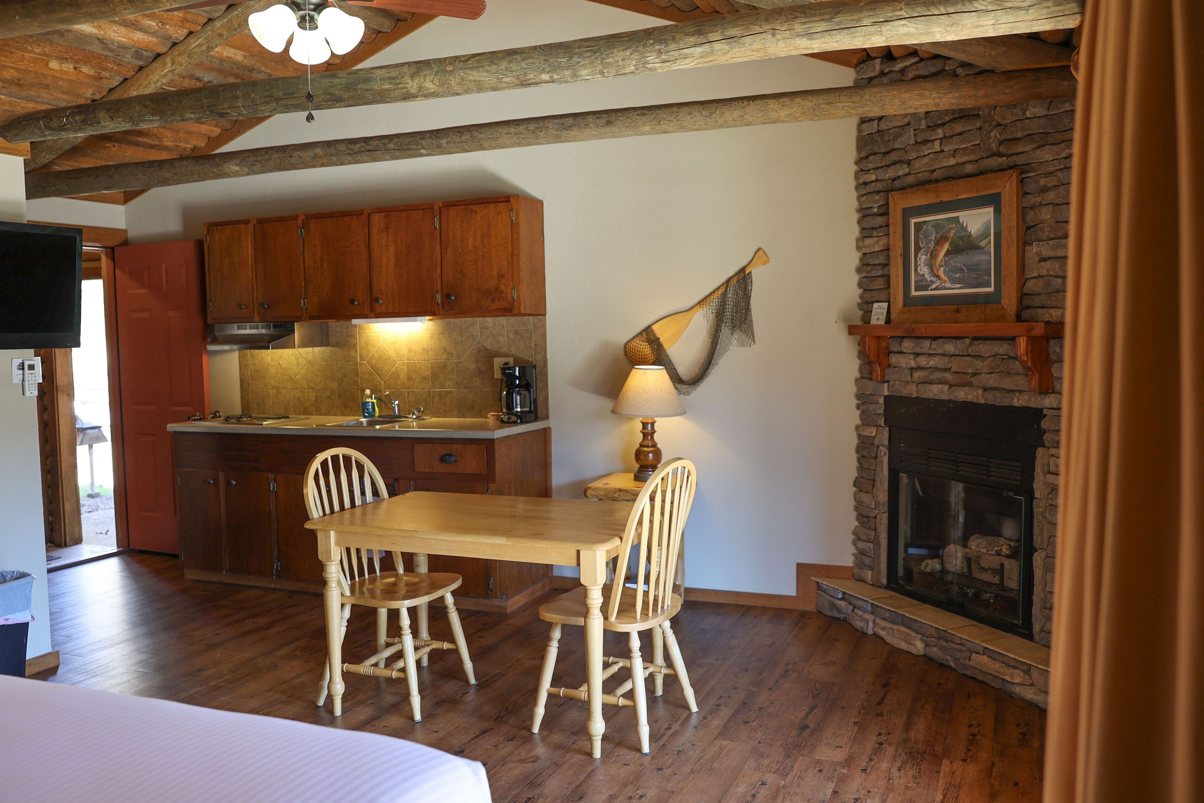 Een rustiek interieur met een houten eettafel, stoelen, een open haard en een keukenhoek.
