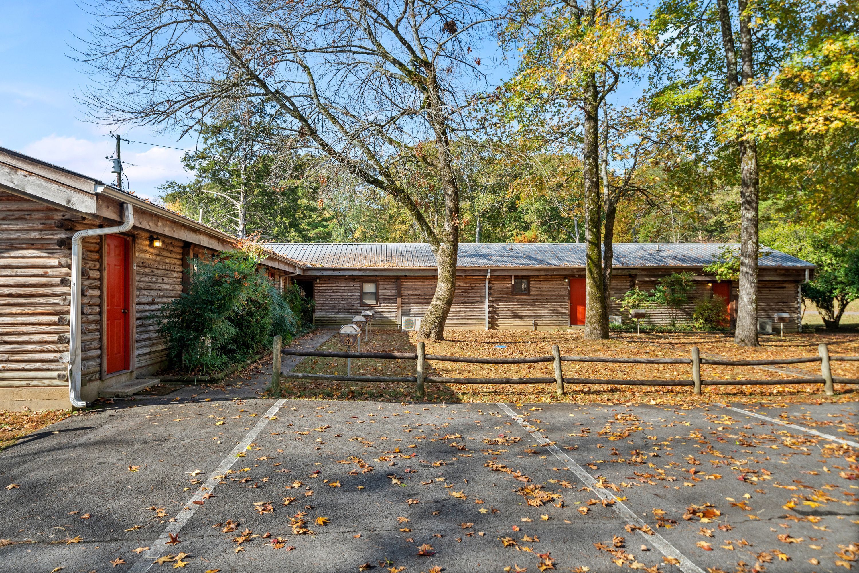 Un chalet rustique avec une porte rouge, un espace de stationnement couvert et une clôture en bois.