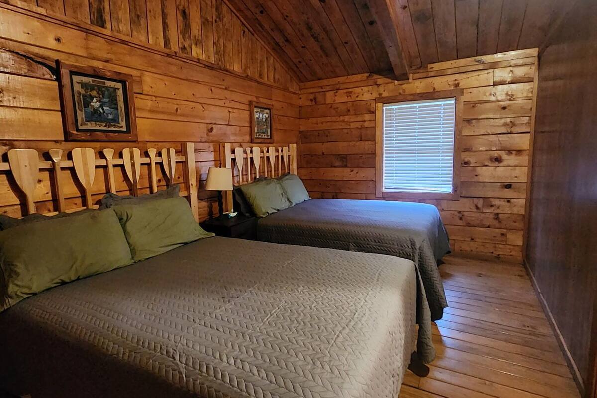 A cabin with two beds, wooden walls, and a window.