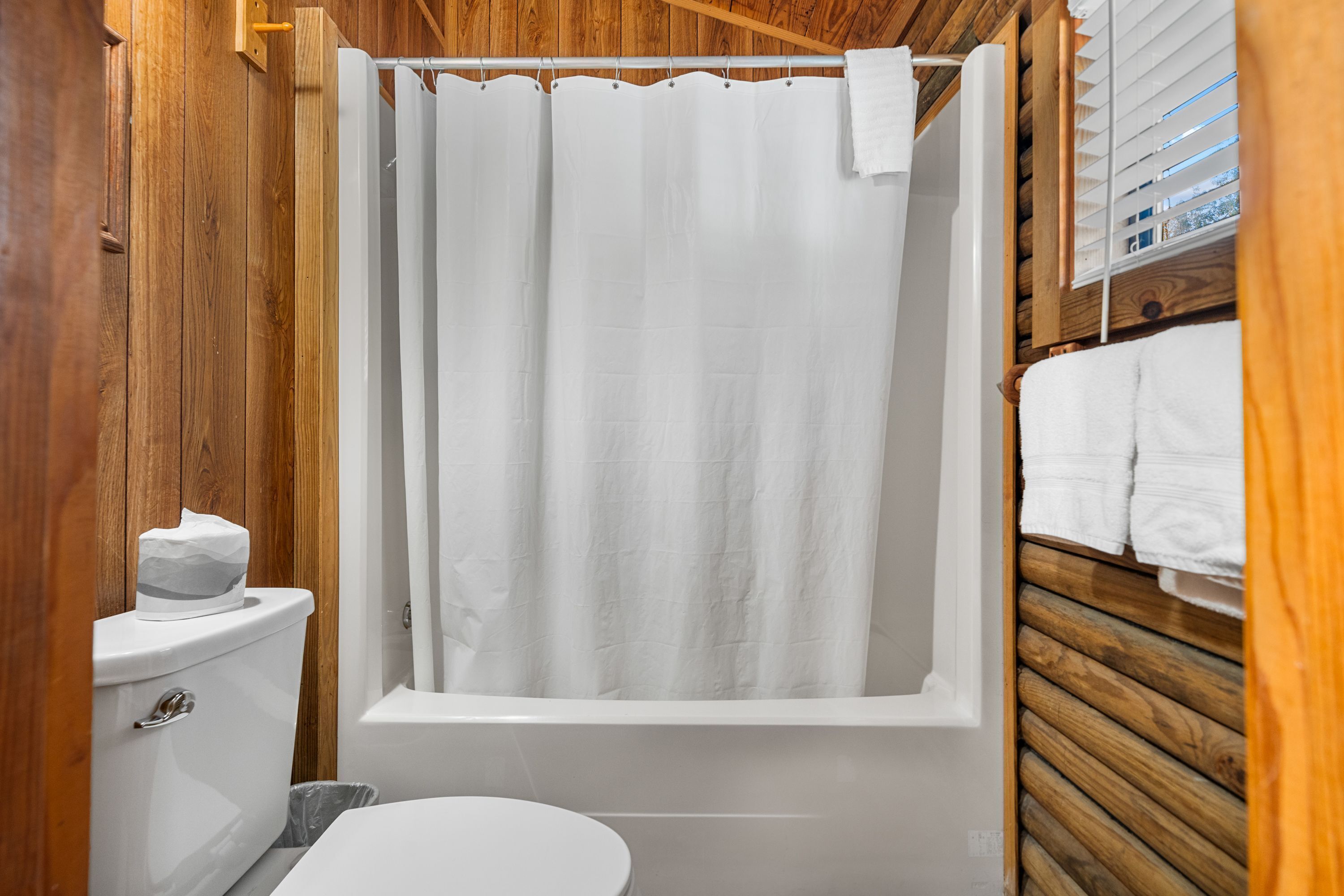 A wooden-paneled bathroom with a bathtub, toilet, and a towel rack.