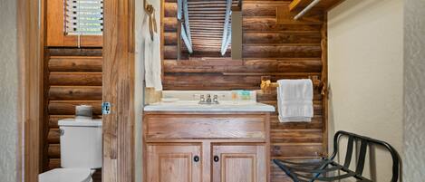 A wooden cabin-style bathroom with a toilet, wooden cabinets, a sink, and a hanging towel rack.