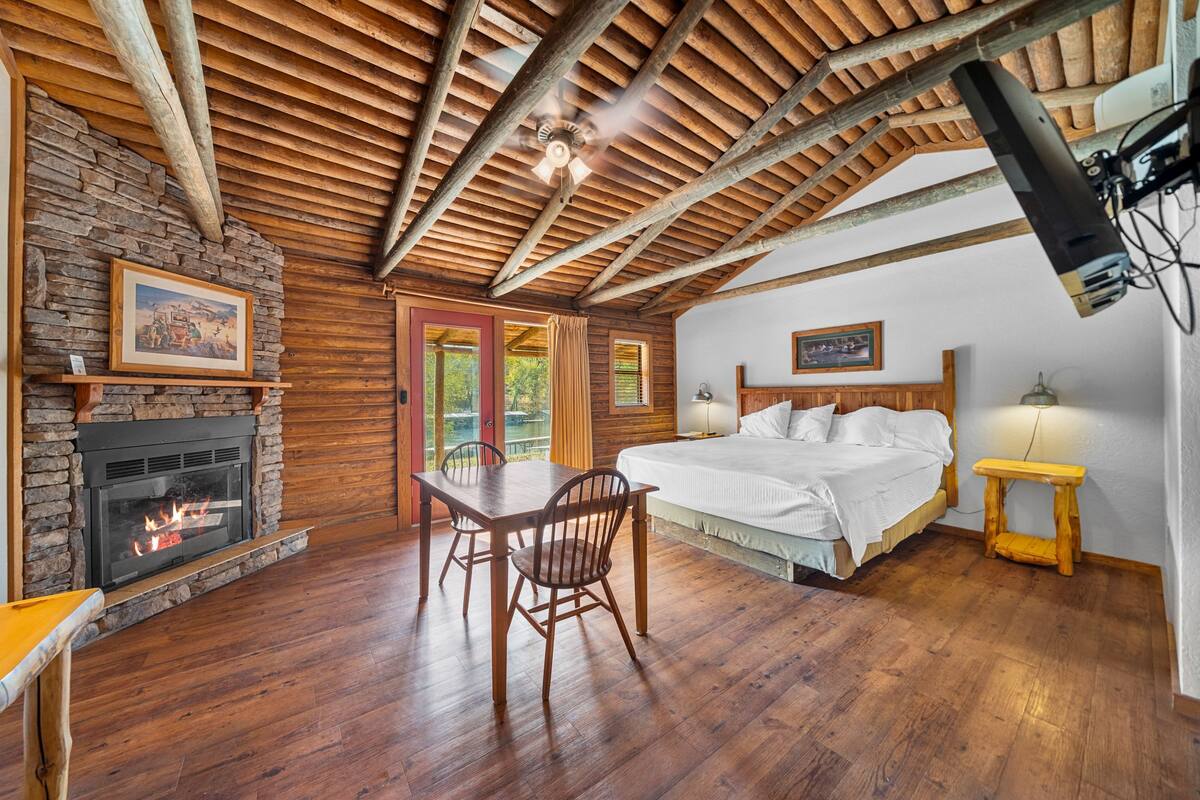 A room with a fireplace, wooden ceiling beams, a bed, and a dining table.