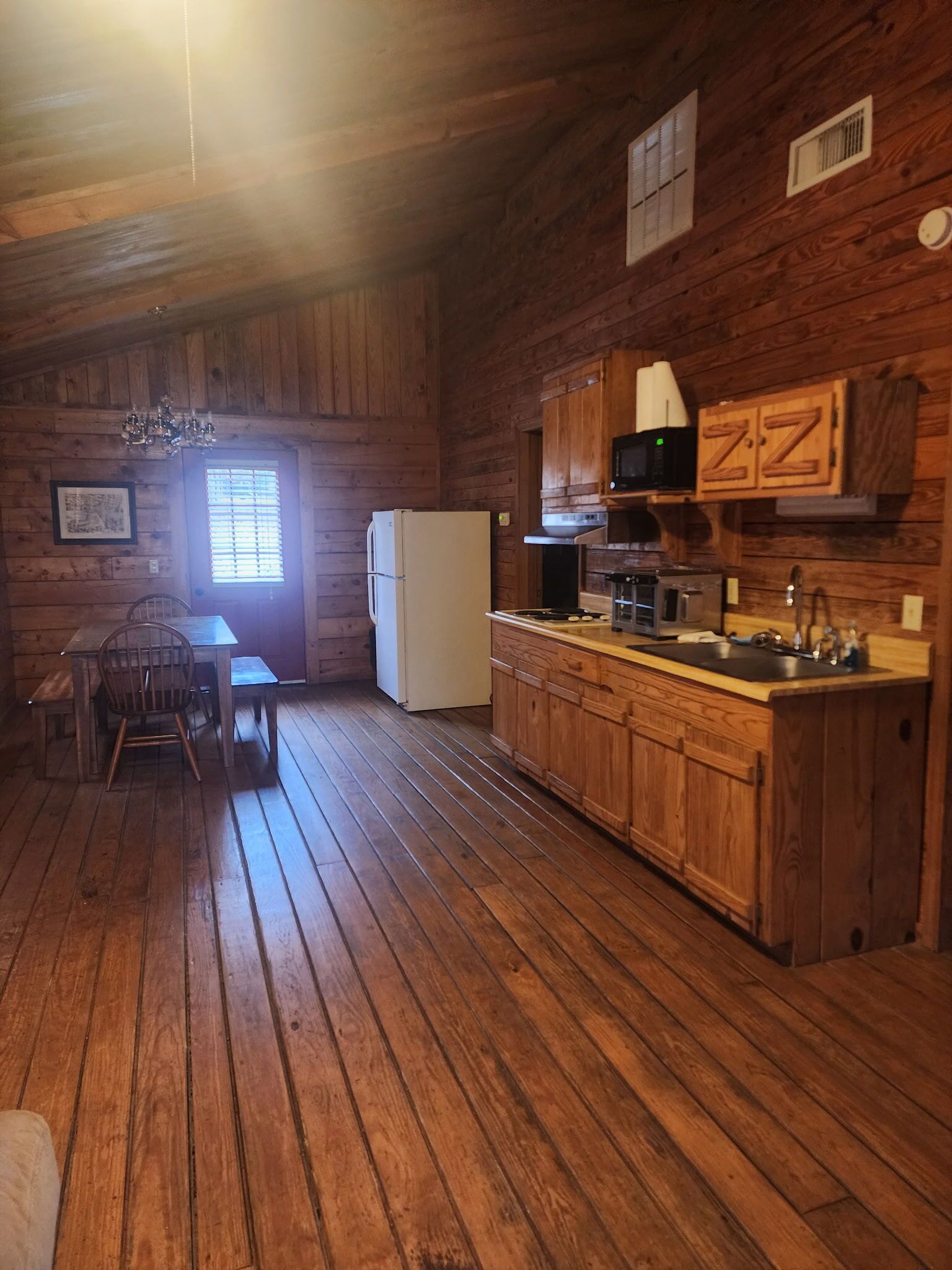Interior de una cabaña de madera con una mesa de comedor, sillas, un refrigerador, una estufa y armarios de madera.