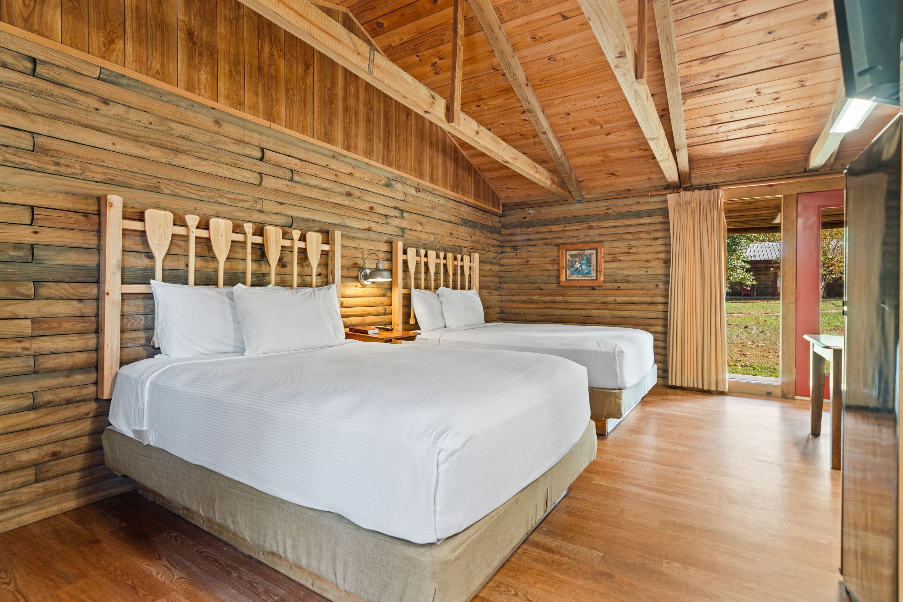 A wooden cabin-style room with two beds, a wooden ceiling, and a view of the outdoors.