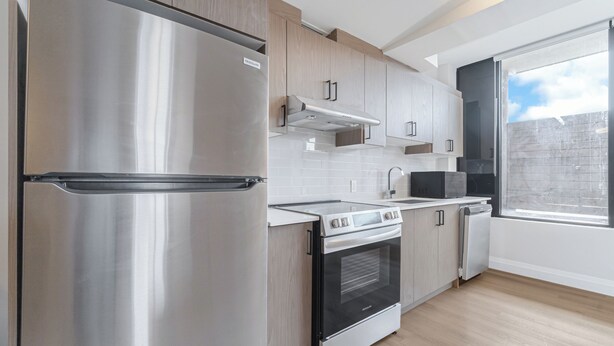 A modern kitchen with stainless steel appliances, wooden cabinets, and a large window. - Unit 3 - Modern Fully Furnished 3 Bedroom Apartment (Toronto)