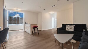 A modern living room with a black sofa, a white coffee table, and a red stool. - Unit 3 - Modern Fully Furnished 3 Bedroom Apartment (Toronto)