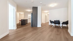A spacious living area with hardwood flooring, a central column, and a dining area with chairs. - Unit 3 - Modern Fully Furnished 3 Bedroom Apartment (Toronto)