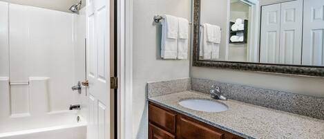 A bathroom with a bathtub, a sink, a mirror, and wooden cabinets.