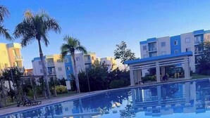 Ein modernes Hotel mit Pool, Palmen und mehrstöckigen Gebäuden im Hintergrund.