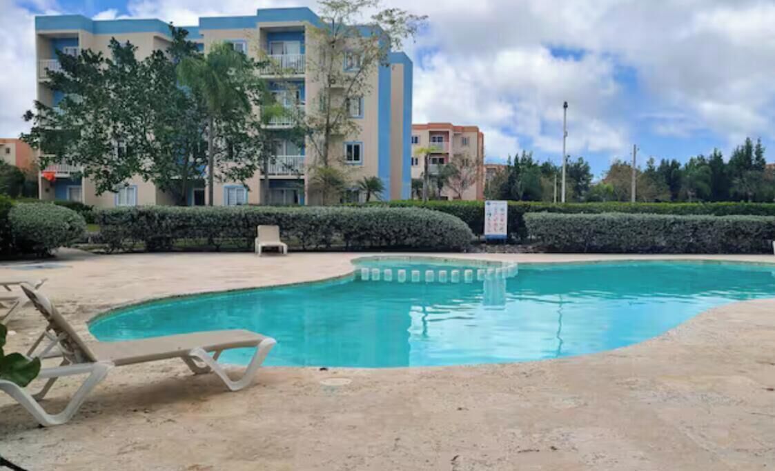 Una piscina con lettini, un edificio con balconi e cielo sereno.