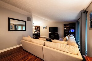 A living room with a sectional sofa, a flat-screen TV, and a bookshelf. - Gorgeous 3-bedroom house with 2nd living rooms in charming Roswell (Roswell)
