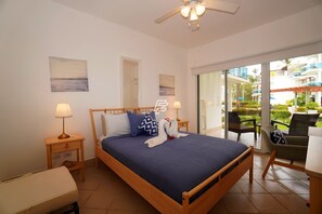 A bedroom with a bed, bedside lamps, a wooden headboard, a window with a view of a balcony, and a ceiling fan. - Beach Paradise: 2-bedroom condo in delightful Las Terrenas with AC (Las Terrenas)