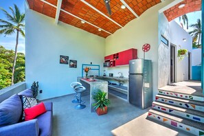 Eine kleine Küche mit einem Kühlschrank, einem Barhocker und einem Essbereich mit einer Couch.
