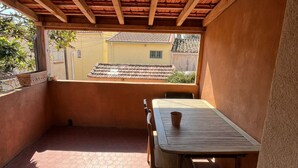 Un porxo cobert amb taula i cadires de fusta, un paviment de rajoles i vista d'un edifici groc al fons.