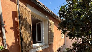 Un edifici amb una finestra, persianes i un balcó amb plantes en testos.