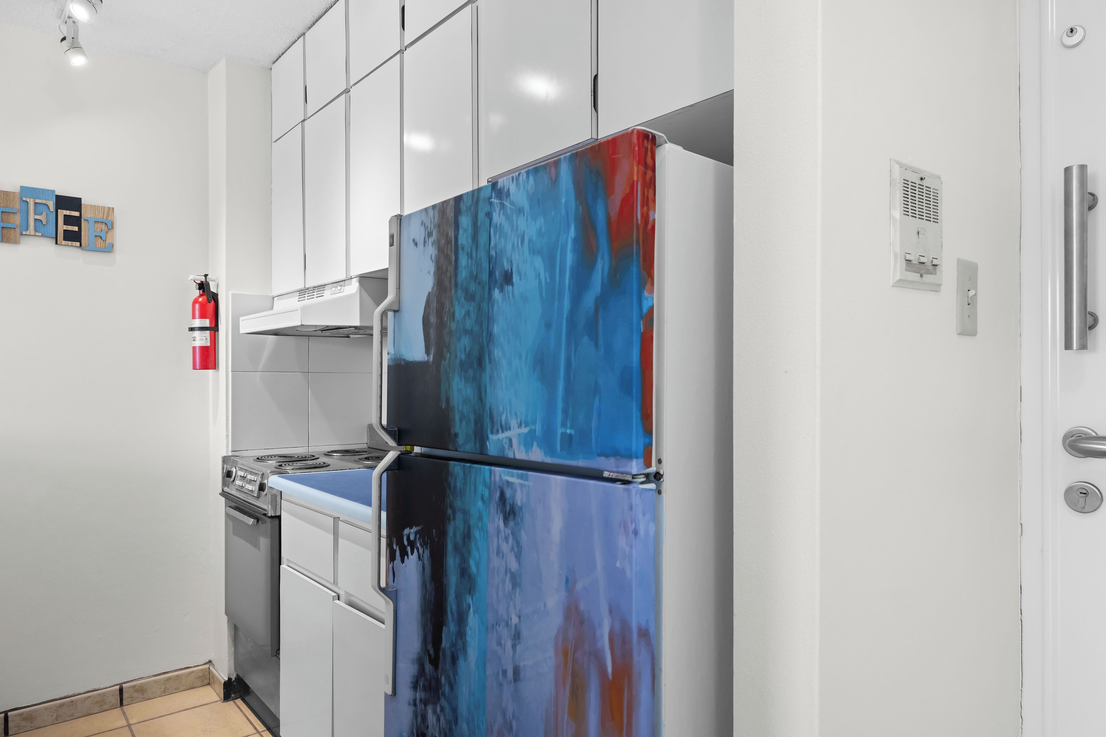 A modern kitchen with white cabinets, a stainless steel stove, and a colorful refrigerator.