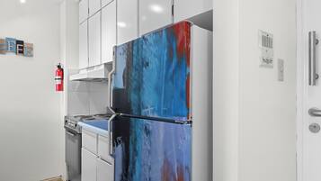 A modern kitchen with white cabinets, a stainless steel stove, and a colorful refrigerator.