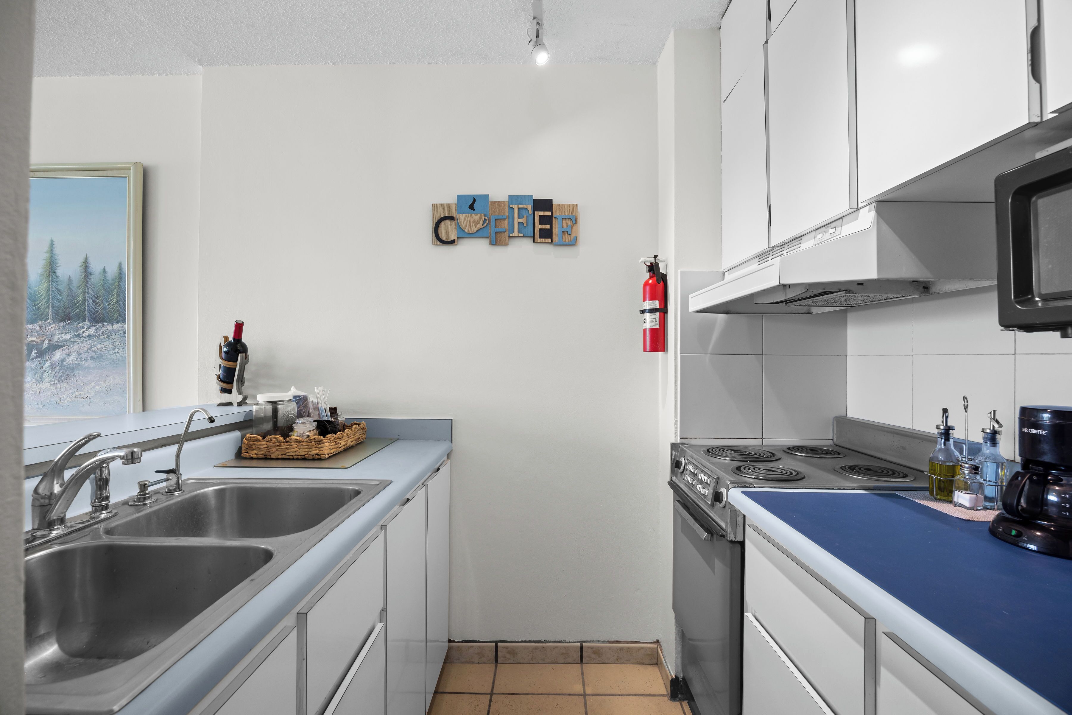 A kitchen with a stove, sink, and a coffee-themed wall decoration.