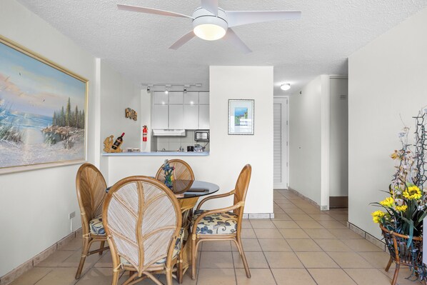 A dining area with wicker chairs, a table, a ceiling fan, and a kitchen in the background. - Playa Azul by Otium (Luquillo)