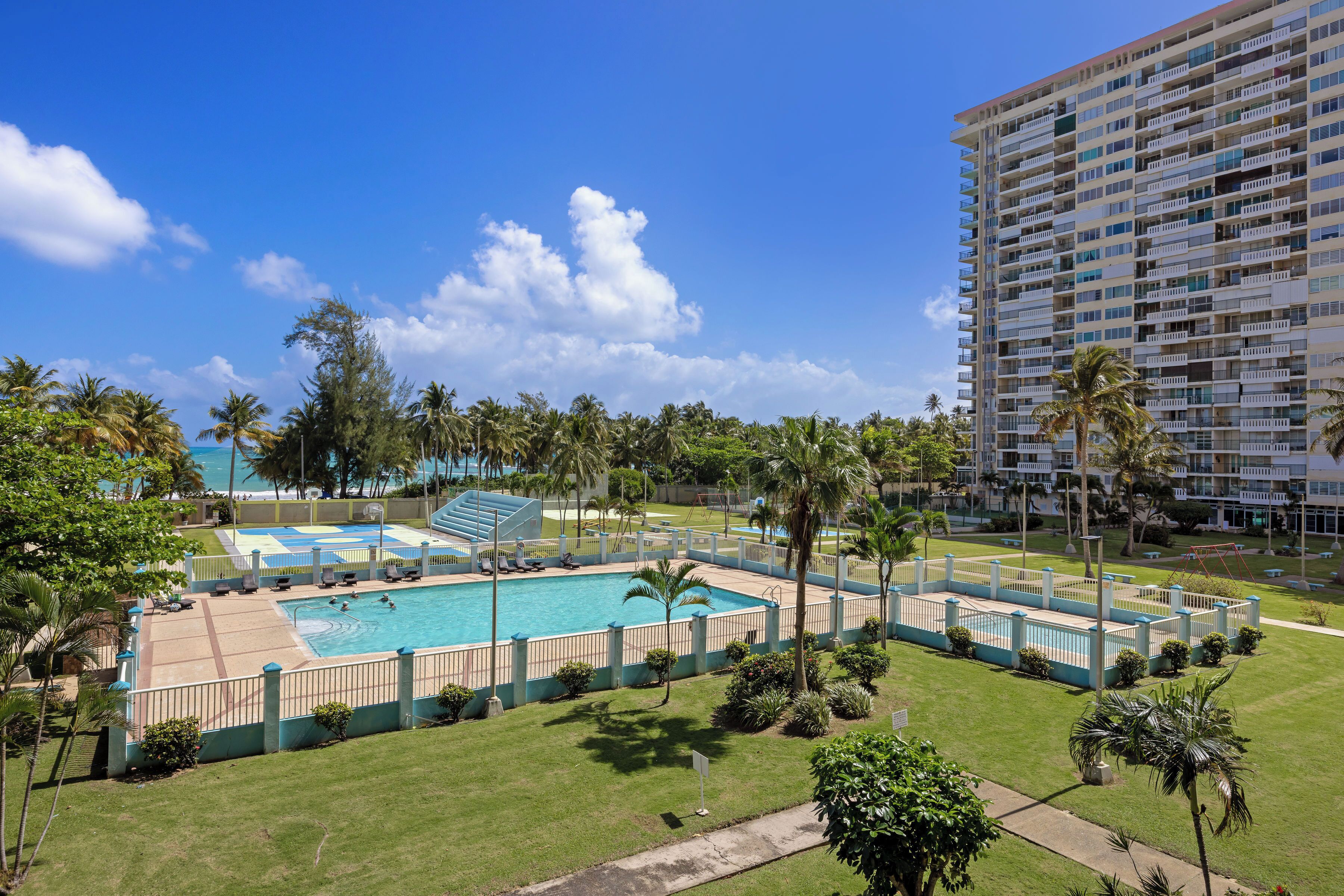 A hotel with a swimming pool, palm trees, and a large building in the background.
