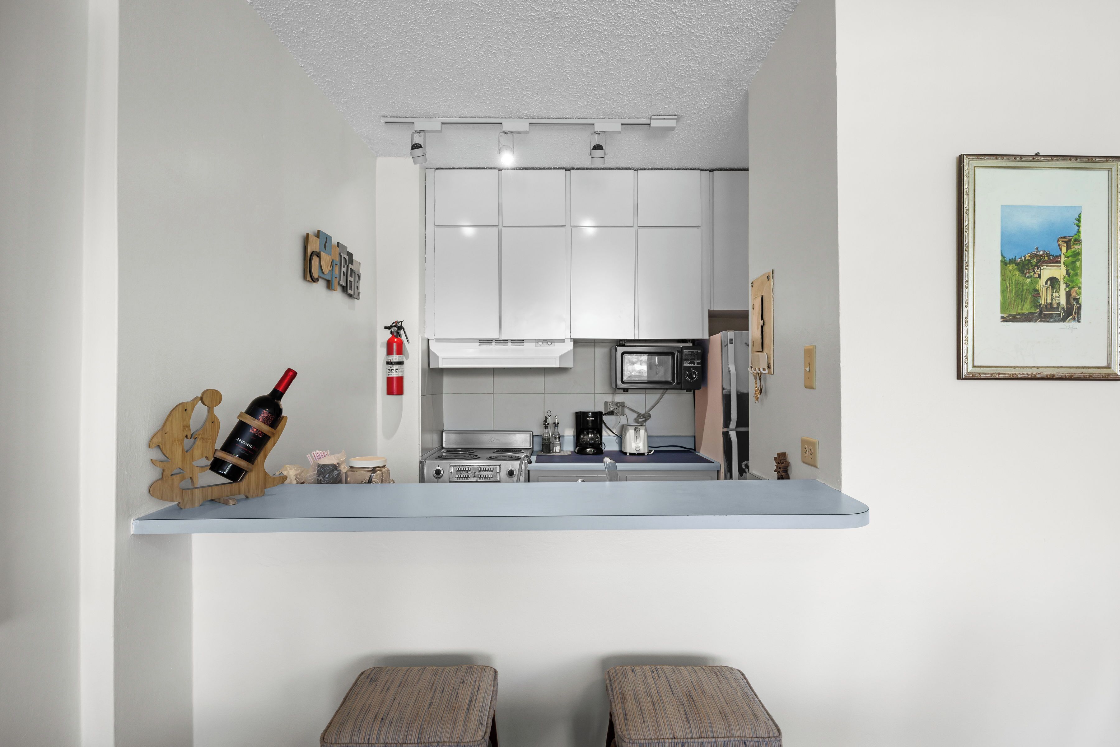 Una cocina compacta con gabinetes blancos, un microondas, una estufa y una pequeña encimera.