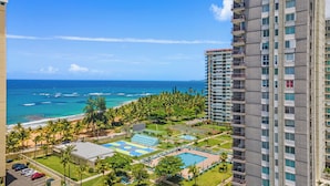 A high-rise hotel with a view of the ocean, a pool area, and a parking lot.