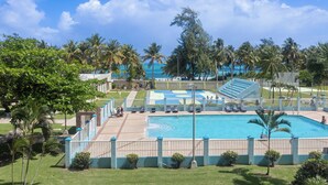 A swimming pool with a blue and white deck, surrounded by palm trees and a clear sky.
