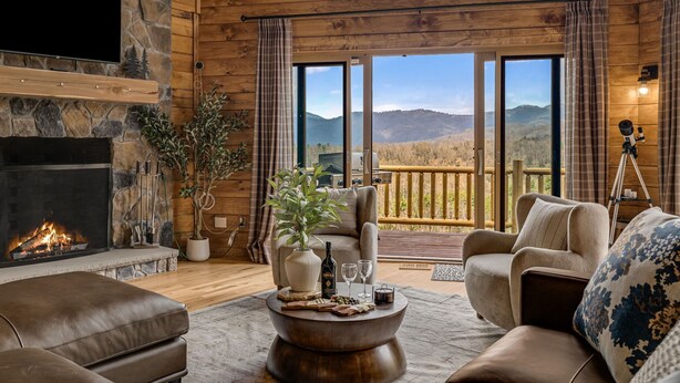 Una sala de estar acogedora con chimenea, asientos cómodos, un ventanal con vistas a la montaña y un balcón.
