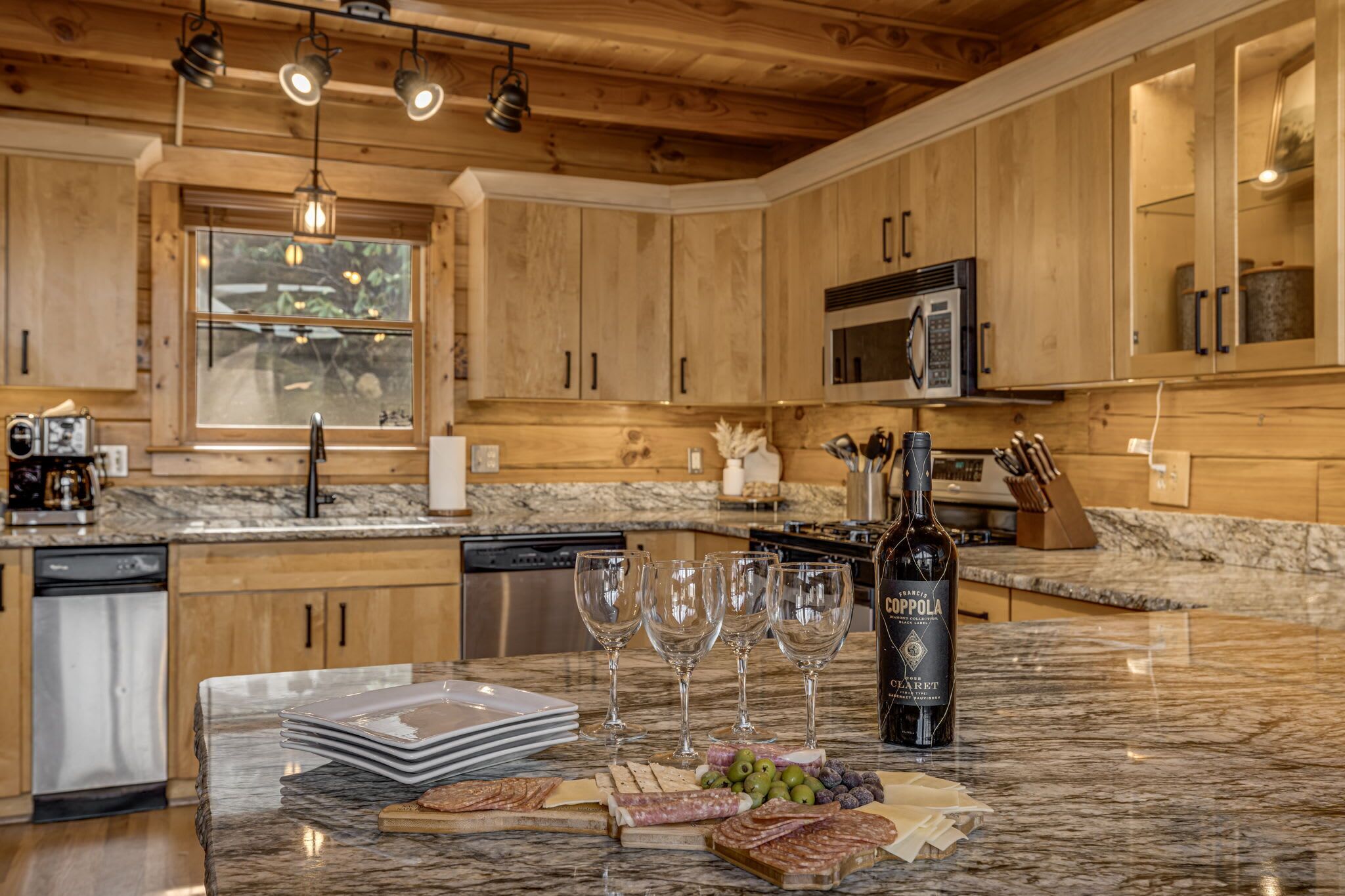 Une cuisine avec des meubles en bois, un plan de travail en granit, une bouteille de vin et des verres à vin.