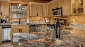 Una cocina con armarios de madera, encimera de granito, una botella de vino y copas de vino.