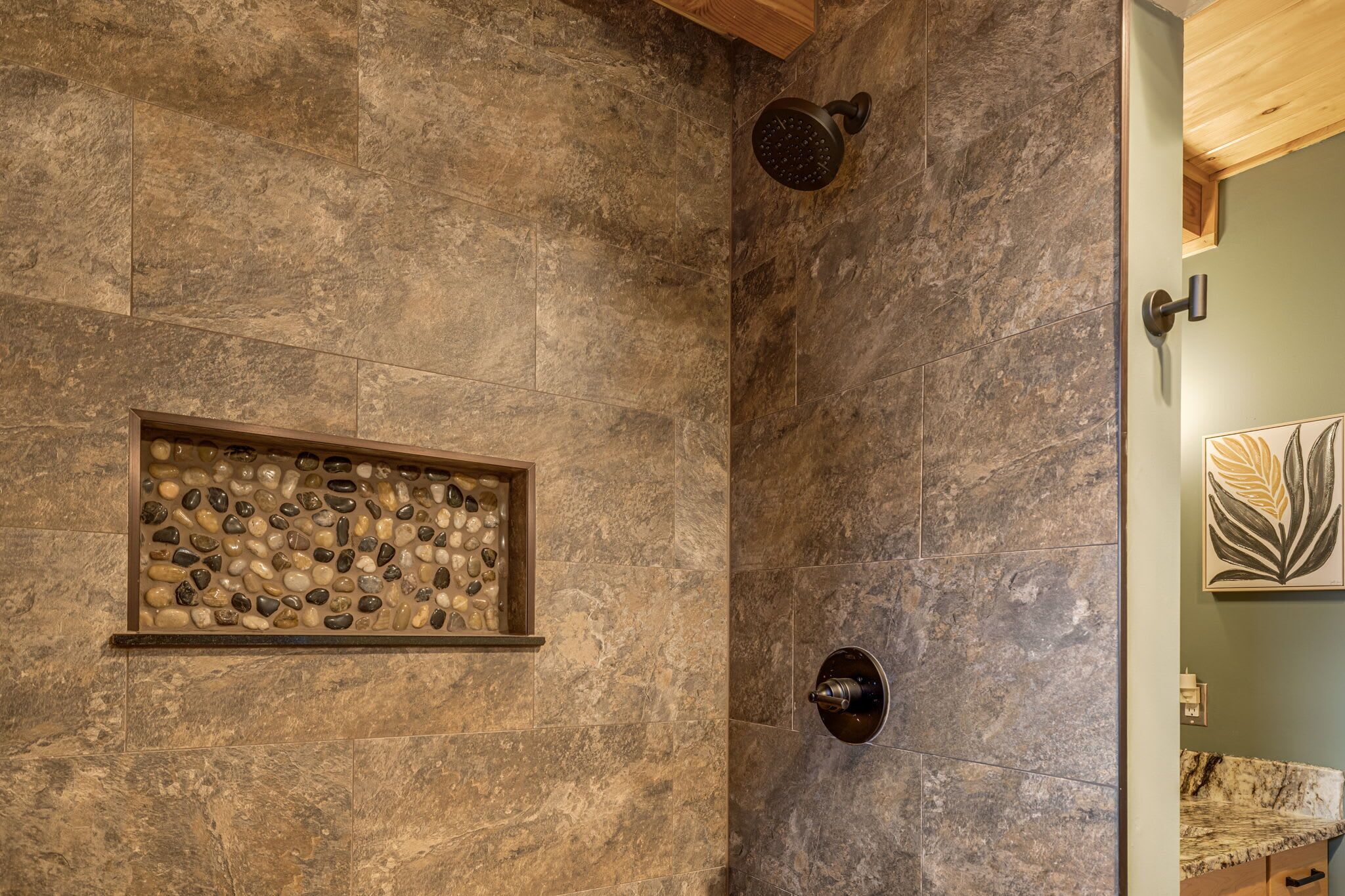 Une salle de bain avec un mur en pierre, une douche dotée d’un pommeau rond et une étagère ornée de pierres décoratives.