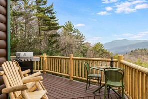 A wooden deck with a grill, chairs, and a table with a bottle. - Private Retreat w/ Views, Hot Tub + Game Room (Lenoir)