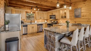 Una cocina con armarios de madera, encimeras de granito, una isla central con taburetes de bar y un salpicadero de piedra.