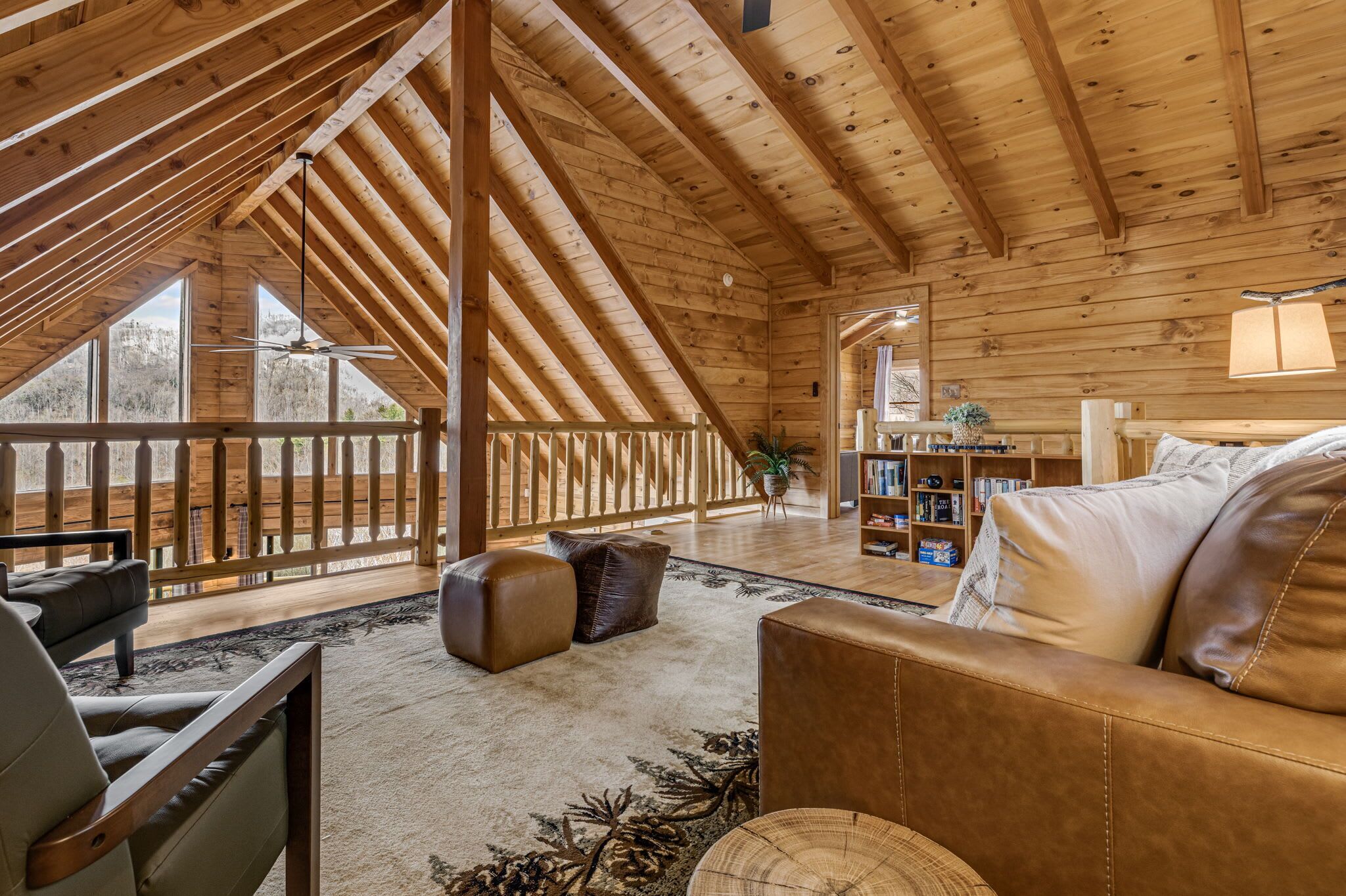 A wooden interior with a high ceiling, a sofa, a bookshelf, and a view through large windows.