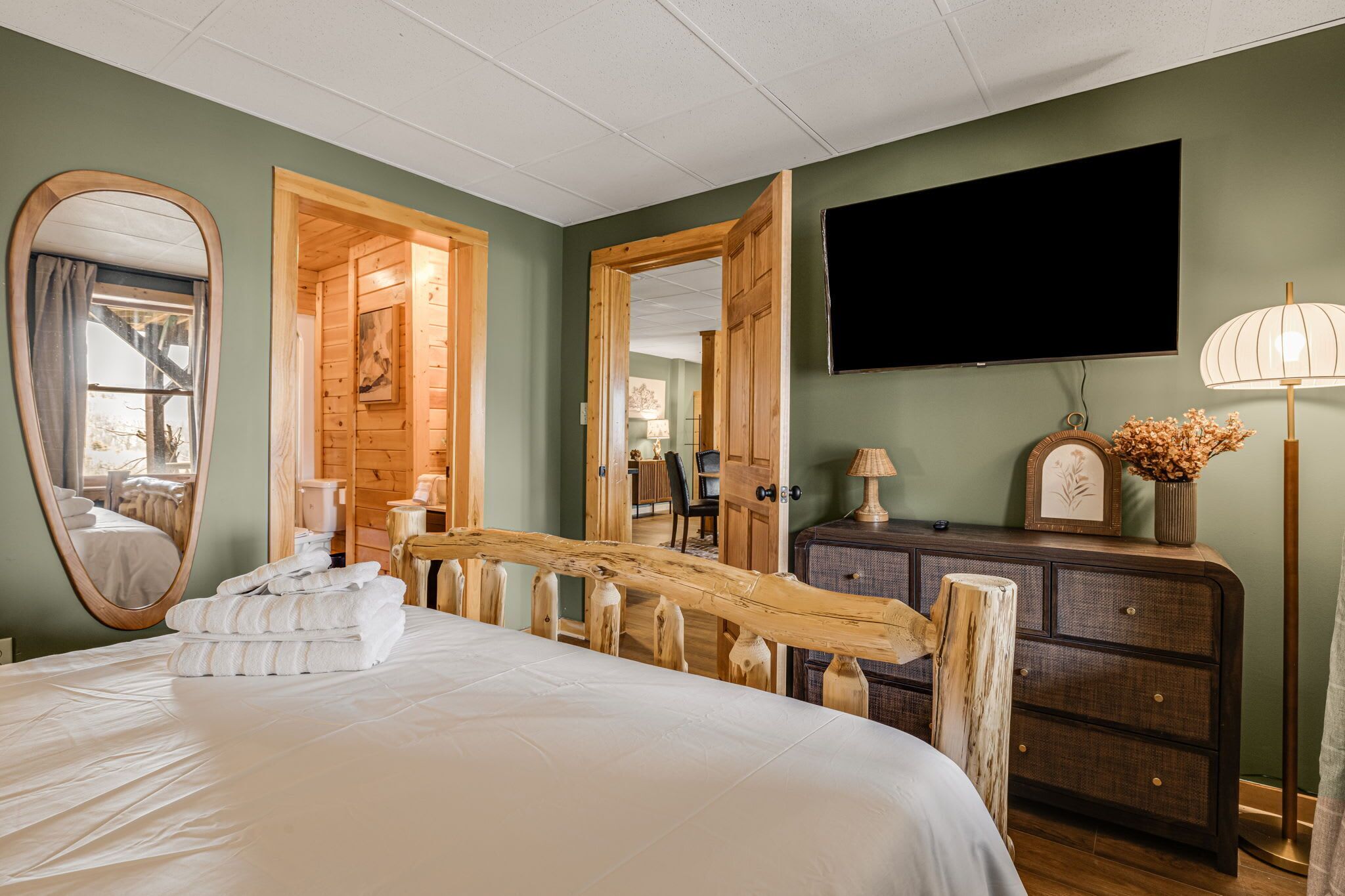 A bedroom with a bed, a mirror, a dresser, a TV, and a wooden chair.