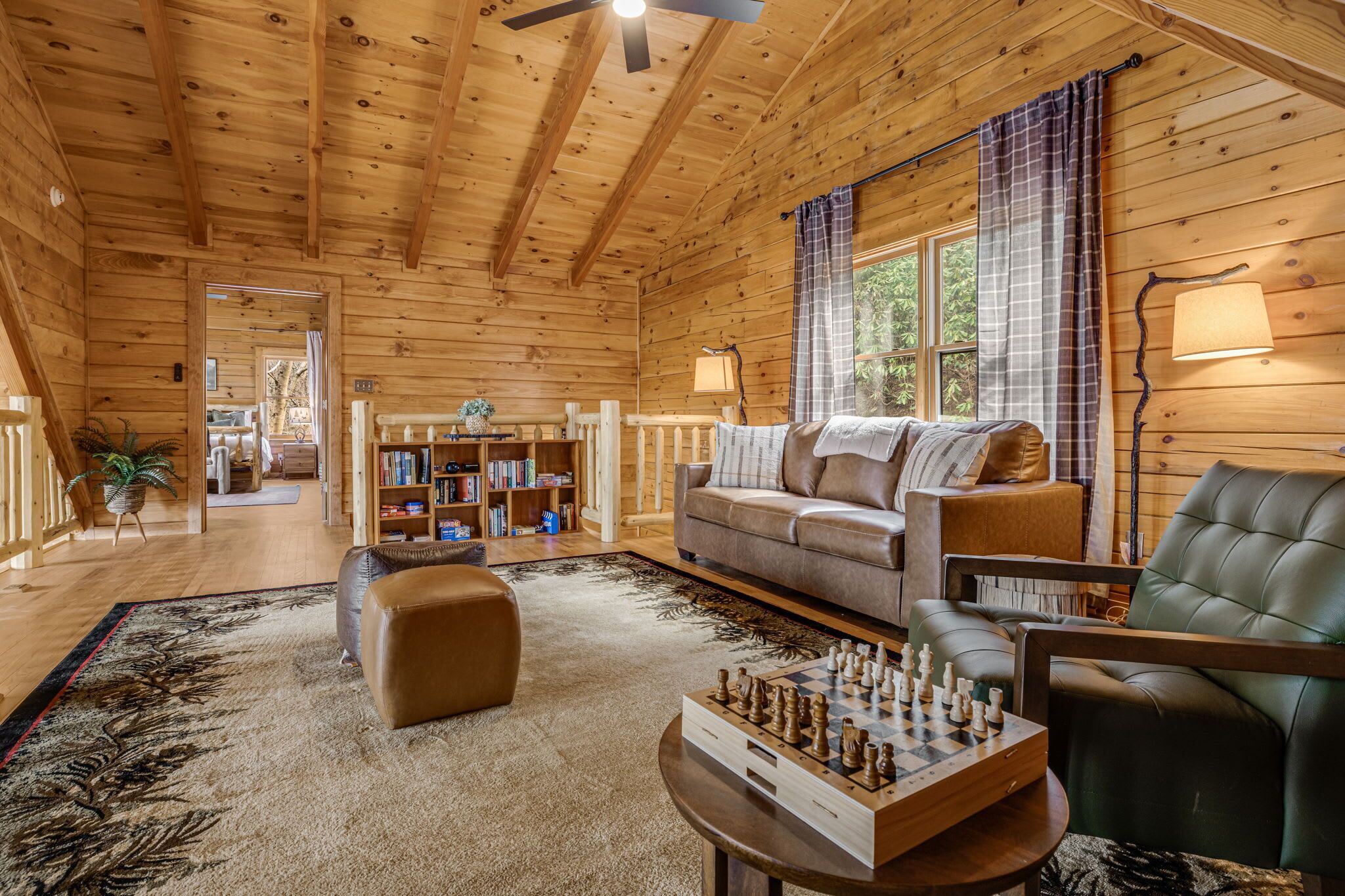 Ein gemütliches Holzhaus-Interieur mit einer Couch, einem Ledersessel, einem Schachbrett und einem Bücherregal.
