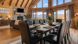 Una habitación amplia con techo alto, ventanas grandes, chimenea y zona de comedor preparada para una comida.