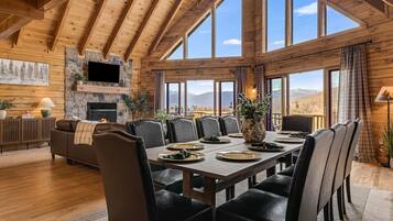 A spacious room with a high ceiling, large windows, a fireplace, and a dining area set up for a meal.
