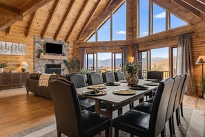Ein geräumiger Raum mit hohen Decken, großen Fenstern, einem Kamin und einem Essbereich, der für eine Mahlzeit gedeckt ist.