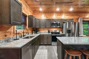 A modern kitchen with granite countertops, stainless steel appliances, and wooden paneling. - 4 Bed Cabin great for multi generational families - Heated Indoor Pool & Games (Sevierville)
