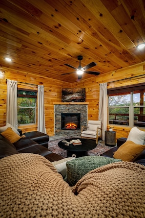 A cozy cabin interior with a fireplace, leather sofas, and a ceiling fan. - 4 Bed Cabin great for multi generational families - Heated Indoor Pool & Games (Sevierville)