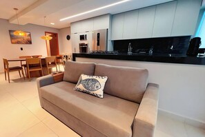 A modern living room with a sofa, a dining table, and a kitchen area with cabinets and appliances. - Urban Gameleira - Miramar Hospedagens (João Pessoa)
