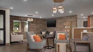 Un hall d’hôtel moderne avec des canapés gris, des éléments décoratifs en bois et un grand téléviseur mural.