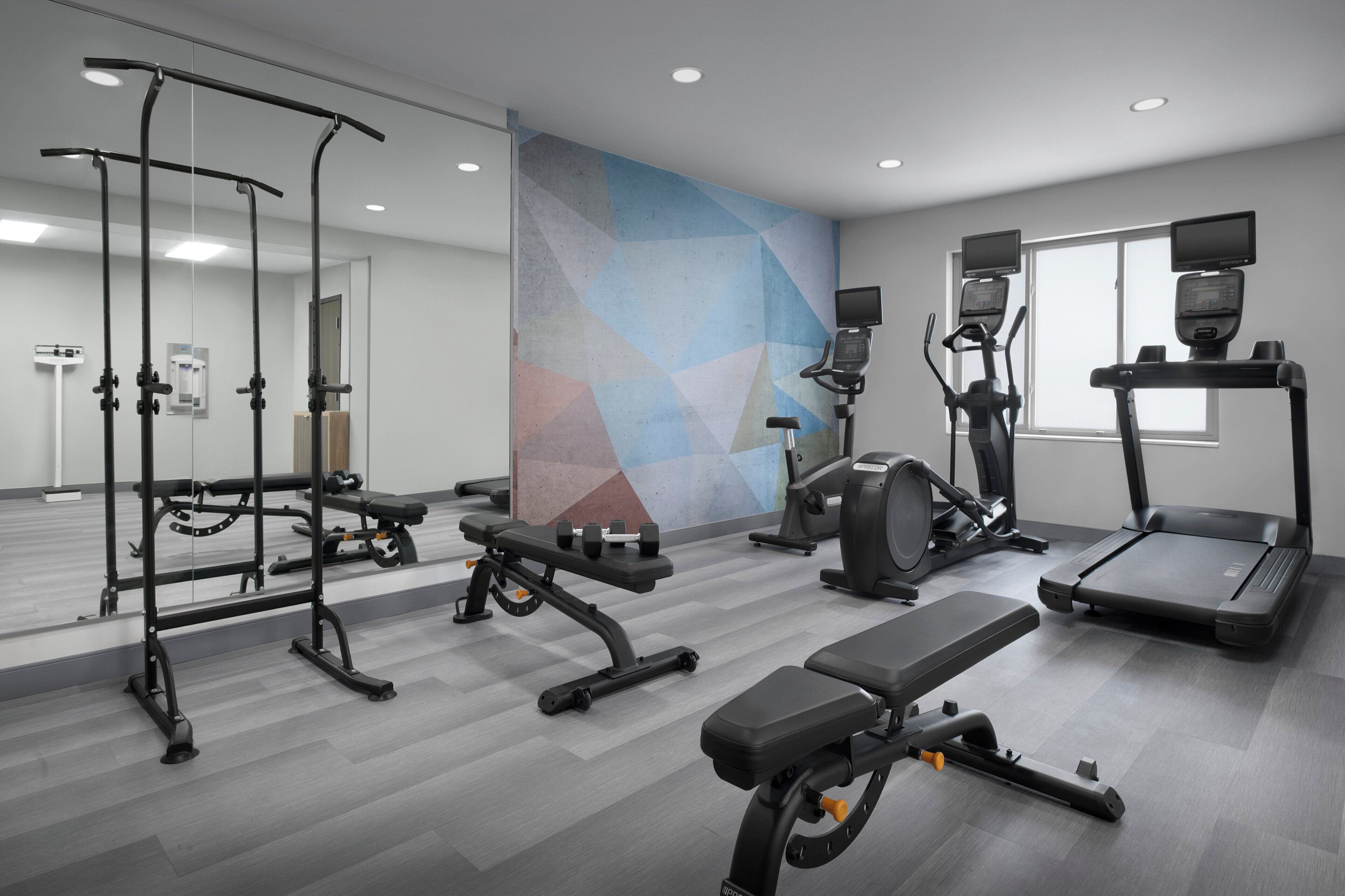 A modern gym with various exercise equipment, including a bench press, elliptical, and treadmills.