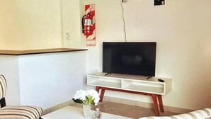 Olohuone, jossa on televisio, raidalliset tuolit, sohvapöytä ja valkoinen kaappi.