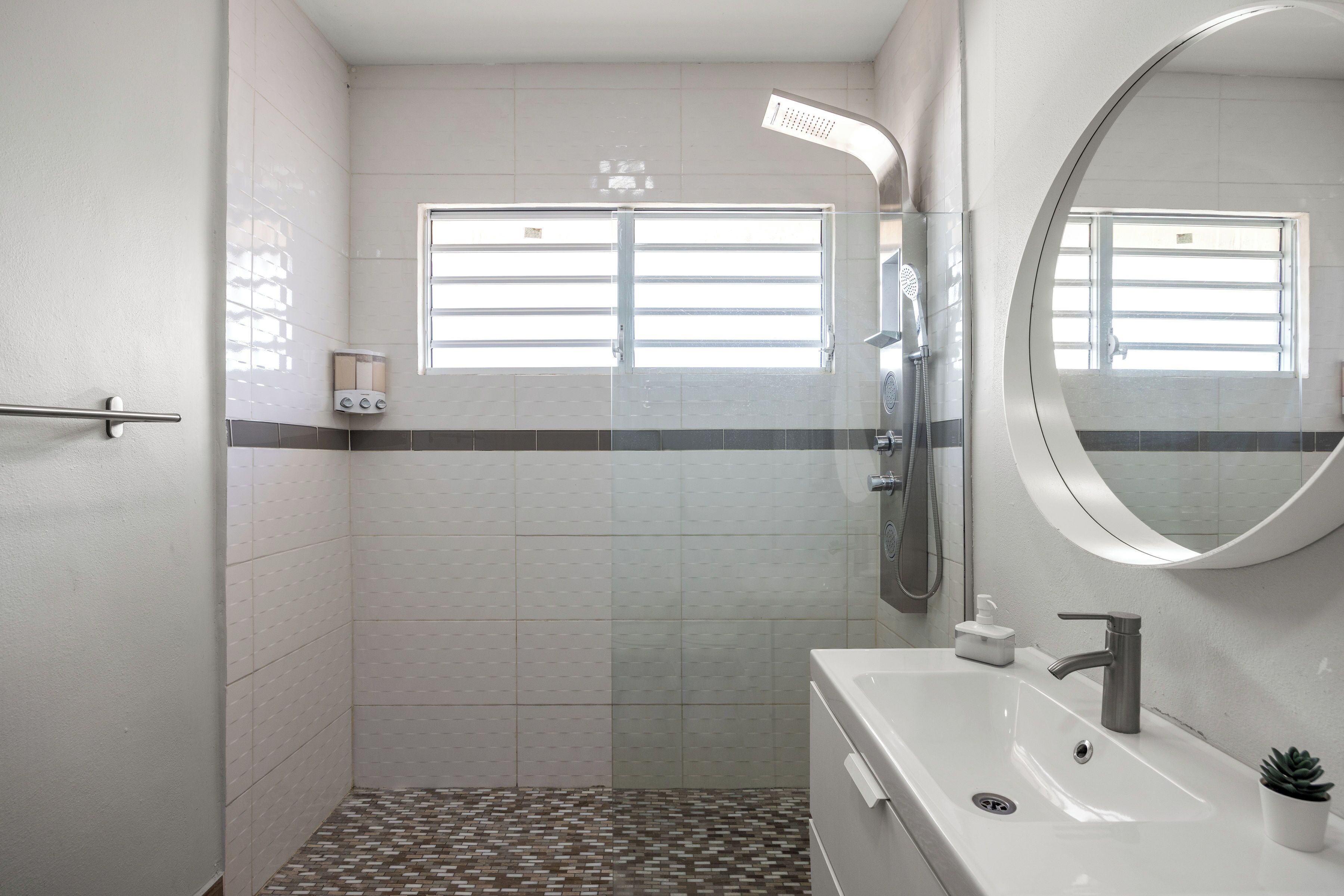 A modern bathroom with a shower, a sink, a mirror, and a window.